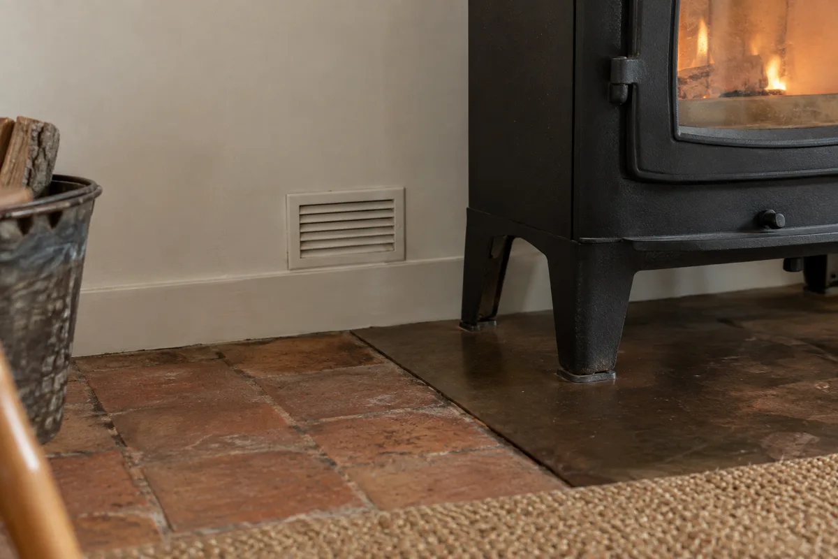 Grille d&rsquo;aération discrète en bas de mur à côté d&rsquo;un poêle à bois