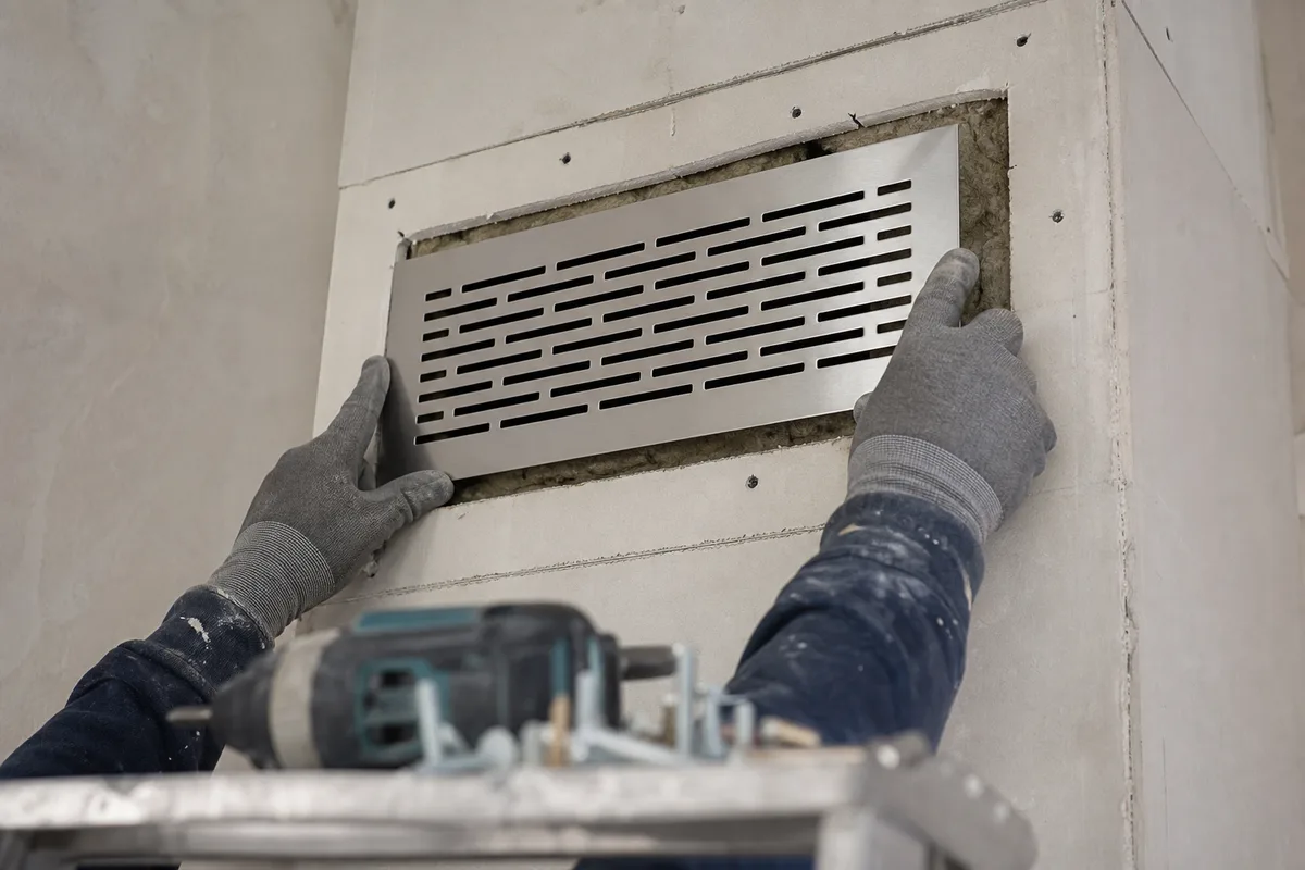 Détail de fixation d’une grille de ventilation haute dans une hotte de cheminée en cours de rénovation
